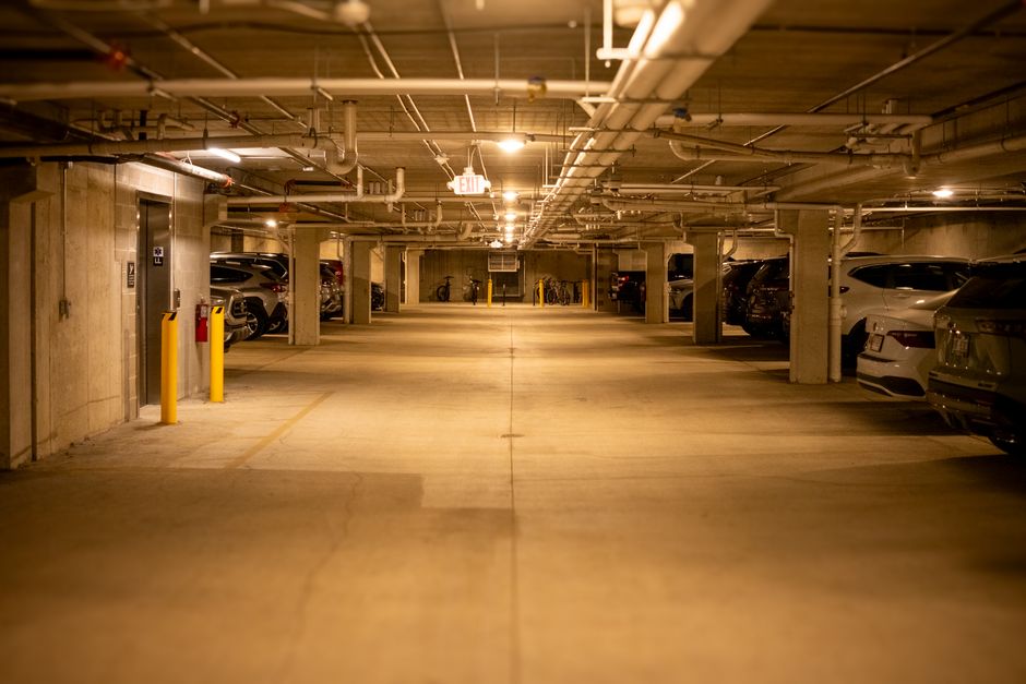 Spacious underground parking garage with cars, pipes, and lights in a dimly lit setting.