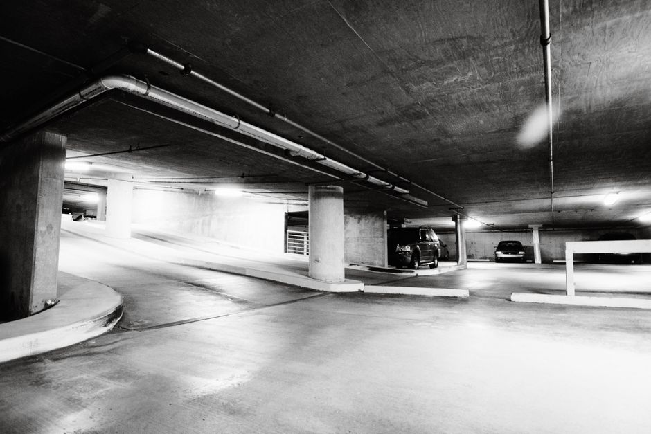 Black and white photo of a spacious underground parking garage with cars parked and concrete pillars.