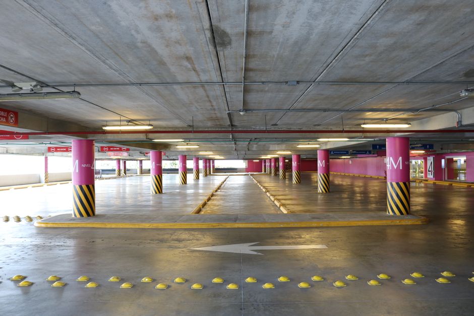 Empty indoor parking deck with pink columns wrapped in black and yellow stripes and a painted arrow on the concrete floor.
